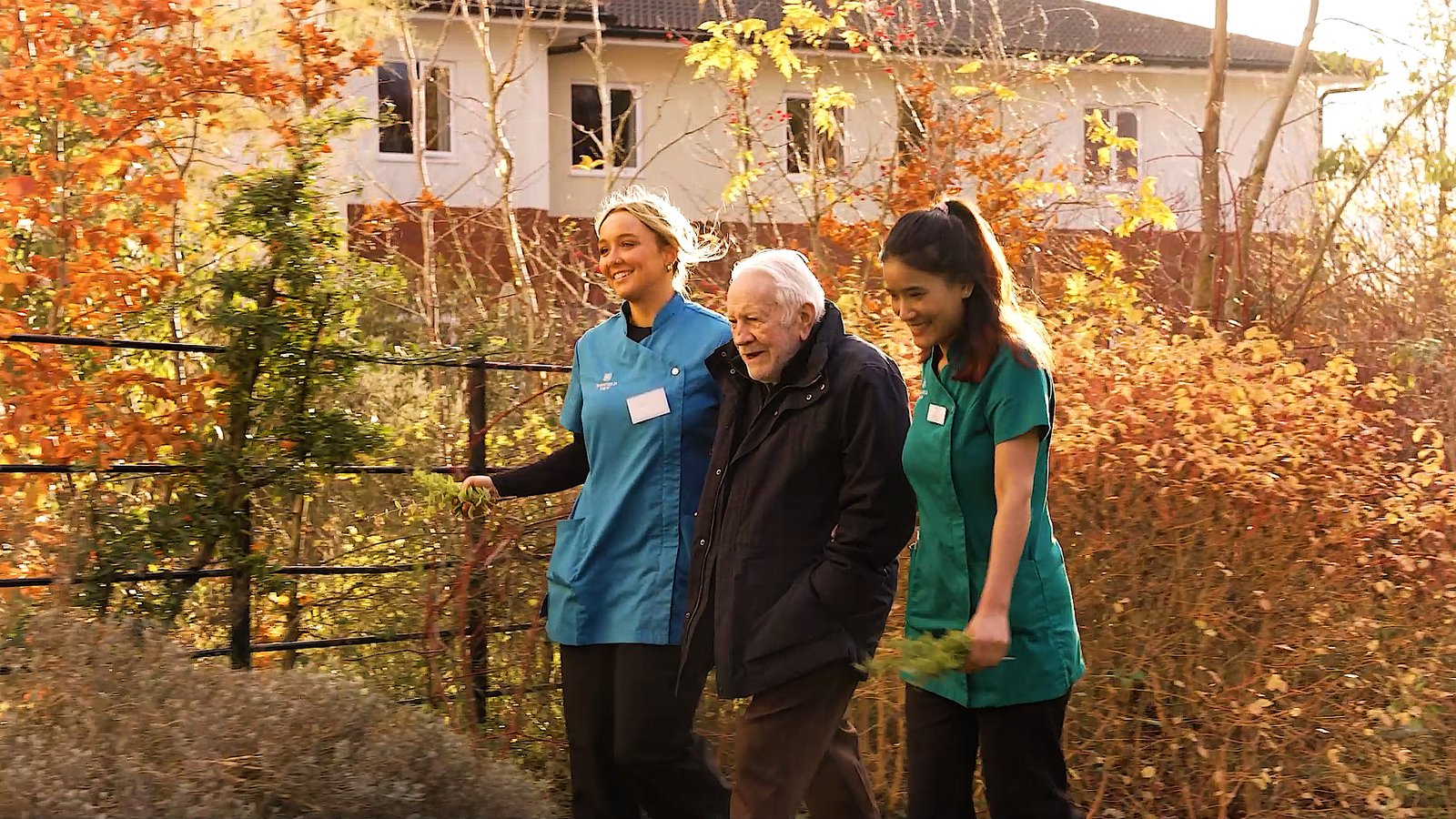 Care home carers walking with resident in garden amber sunset autumn